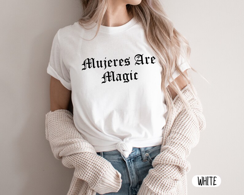 May include: White t-shirt with the text "Mujeres Are Magic" printed in black.