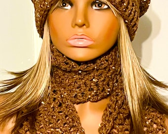 May include: A brown crochet beanie hat and a matching brown crochet scarf featuring an openwork pattern with subtle metallic flecks throughout the yarn. The set is displayed on a mannequin head with blonde hair and light skin tones.