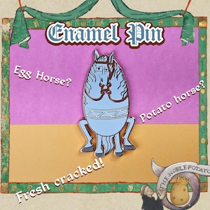 May include: An enamel pin featuring a light blue horse-like figure with brown accents, set against a pink and gold background. The pin has the text "Enamel Pin", "Egg Horse?", "Potato horse?", and "Fresh cracked!" in a medieval style.