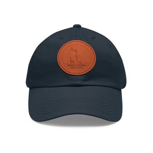 May include: A navy blue baseball cap with a brown leather patch featuring a silhouette of a rock formation and the text "Bryce Canyon National Park".