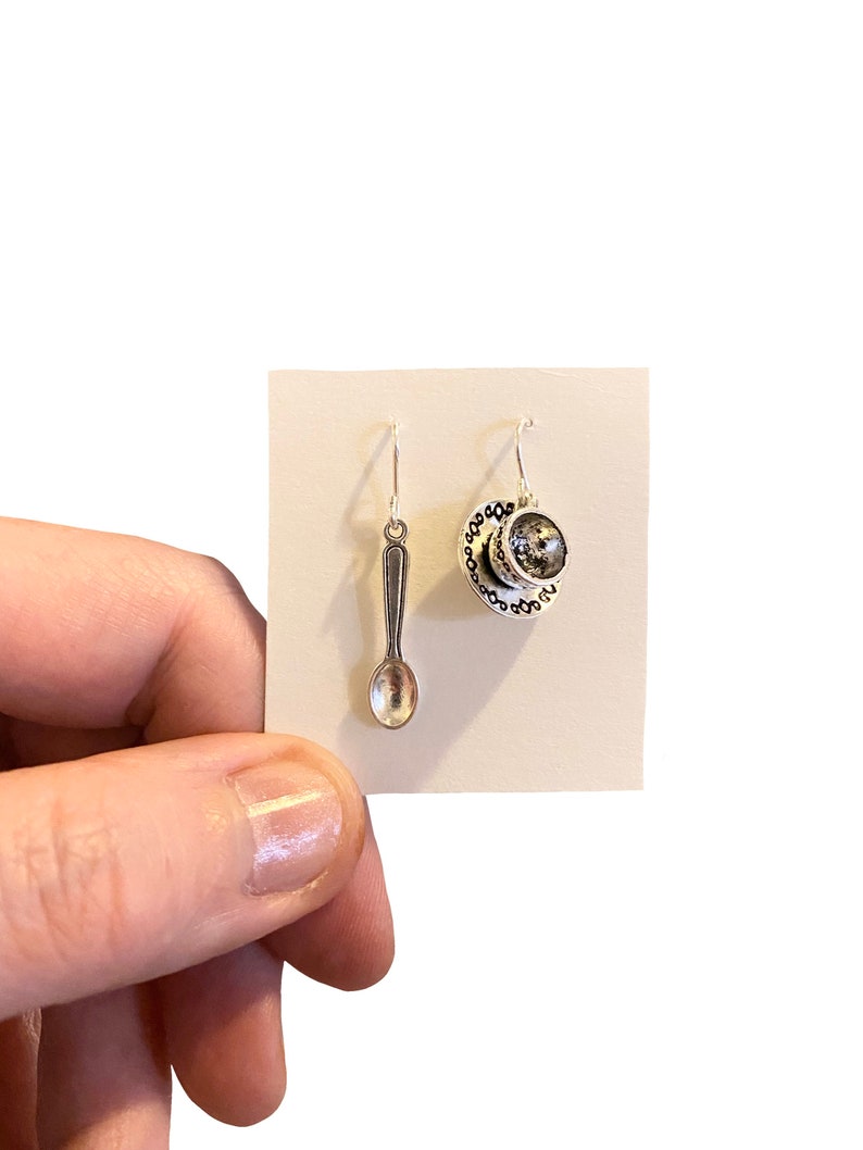 May include: A pair of silver earrings, one shaped like a teacup and saucer, the other shaped like a spoon.