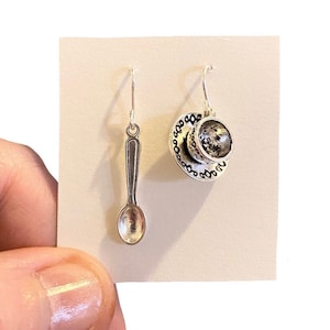 May include: A pair of silver earrings, one shaped like a teacup and saucer, the other shaped like a spoon.