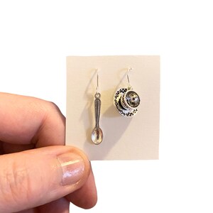 May include: A pair of silver earrings, one shaped like a teacup and saucer, the other shaped like a spoon.