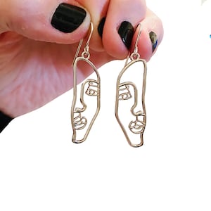 Può includere: Un paio di orecchini d'argento con un disegno a linea di un viso su ogni orecchino.