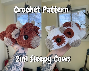 May include: Two crocheted cow plushies, one brown and white, the other white and brown, with sleepy eyes. The plushies are held in a person's hands. The image text reads "Crochet Pattern 2in1 Sleepy Cows".