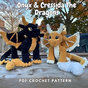May include: Crochet pattern for two plush dragon toys, one black with gold accents and one brown with white accents. The pattern is titled "Onyx & Cressida The Dragons" and is available as a PDF download.