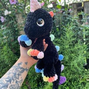 May include: Black crocheted unicorn plush toy with rainbow coloured yarn accents. The unicorn has large, glittery eyes.