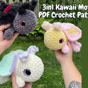 May include: Three crocheted moth plushies in different colours. A black moth with red accents, a yellow moth with pink accents, and a white moth with green and purple accents. The plushies are all being held in hands. The image text reads "3in1 Kawaii Moths PDF Crochet Pattern".