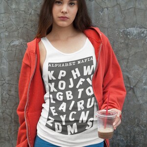 May include: A woman wearing a red hoodie over a white tank top with the text "Alphabet Mafia" and a black and white jumbled letter design. She is holding a clear plastic cup with a red straw.