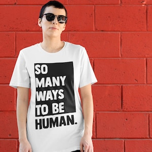 May include: A white t-shirt with a black box on the front that says "SO MANY WAYS TO BE HUMAN."