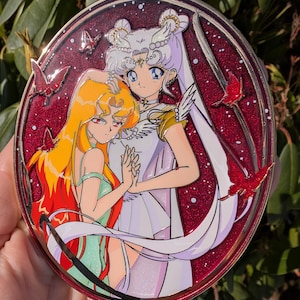 Può includere: Una spilla rotonda in smalto rosso con un design bianco e oro. Due personaggi anime sono raffigurati in un abbraccio stretto. Lo sfondo è un cielo notturno stellato con farfalle rosse.