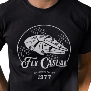 May include: Black t-shirt featuring a white graphic of the Millennium Falcon spaceship from Star Wars. The graphic is in a circle with the text "Fly Casual" and "Millennium Falcon 1977" underneath.