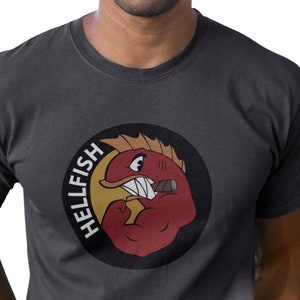 Peut inclure: Un t-shirt gris foncé avec un graphique circulaire d'un poisson de dessin animé rouge avec un cigare dans la bouche. Le texte "HELLFISH" est écrit verticalement autour du poisson.