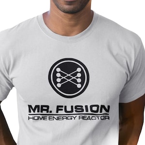 May include: White t-shirt featuring a black and white graphic of a circle with a stylised design inside and the text "MR. FUSION HOME ENERGY REACTOR" underneath.