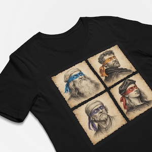 Könnte beinhalten: Ein schwarzes Kurzarm-T-Shirt mit einem Grafikdruck von vier Porträts im Renaissance-Stil. Jede Figur trägt eine farbige Augenmaske in Blau, Orange, Rot oder Lila, dargestellt in einem Raster aus vier einzelnen, quadratischen Rahmen mit Altpapier-Optik.