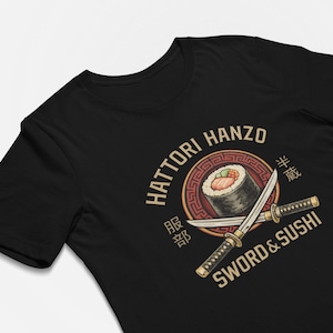 May include: Black t-shirt featuring a graphic design with the text "Hattori Hanzo Sword & Sushi." The design includes a sushi roll, crossed swords, and Japanese text within a circular emblem. The shirt is made of a soft material.
