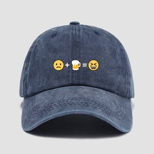 Może przedstawiać: Niebieska denimowa czapka z daszkiem z haftowanym wzorem przedstawiającym żółtą buźkę, znak plus, kufel piwa, znak równości i śmiejącą się buźkę.