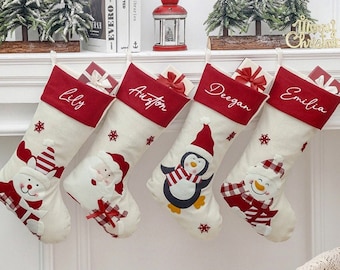 May include: Four Christmas stockings with red cuffs and personalized names: Lily, Auston, Deegan, and Emilia. Each stocking features a different festive character: a snowman, Santa Claus, and a penguin. Small gifts are tucked inside.