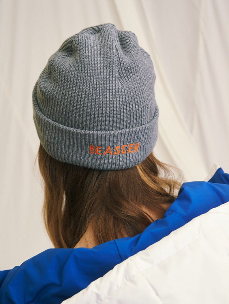 May include: Gray knitted beanie with the text "BE A SEE-ER" embroidered in orange on the back.