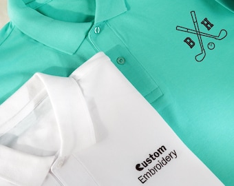 May include: Two polo shirts, one white and one turquoise. The white shirt has the text "Custom Embroidery" on the front. The turquoise shirt has a black embroidered design of two crossed golf clubs with a golf ball.