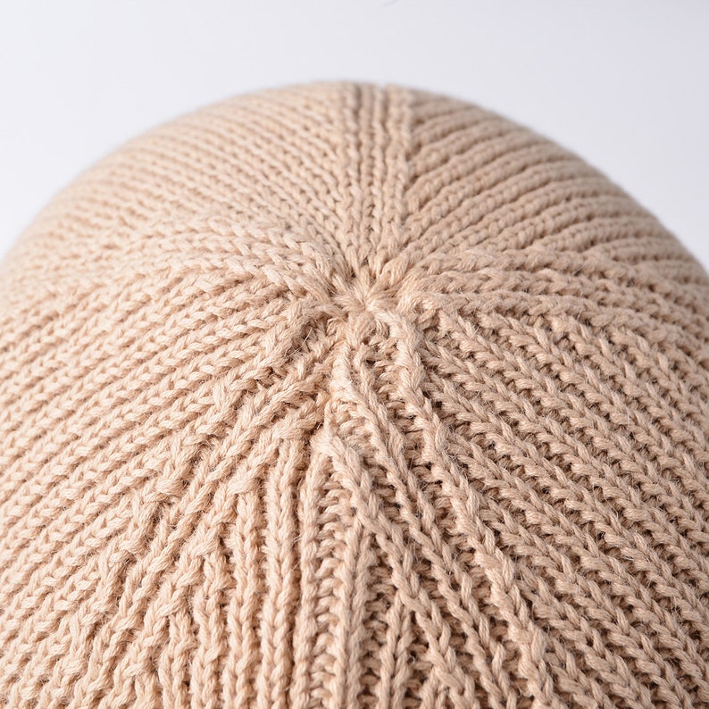 May include: Close-up of a beige knitted beanie hat. The hat is made of a soft, textured yarn and has a simple, classic design.