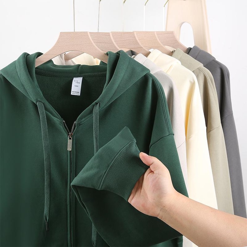 May include: A dark green hooded sweatshirt with a zipper closure. The sweatshirt has a drawstring hood and a tag on the left side of the chest.