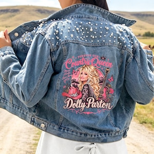 May include: A blue denim jacket featuring white pearl embellishments on the shoulders and a back graphic of Dolly Parton with a pink cowboy hat, guitar, butterflies, and text that reads Forever Our Country Queen Dolly Parton Music Heals Love Lives On.