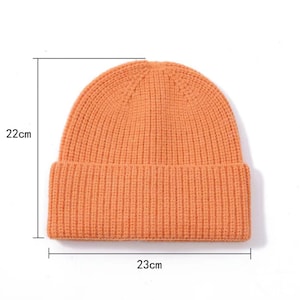 May include: A bright orange knitted beanie with a ribbed texture. The beanie measures 22 cm in height and 23 cm in width.