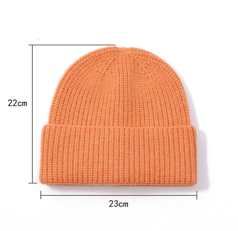 May include: A bright orange knitted beanie with a ribbed texture. The beanie measures 22 cm in height and 23 cm in width.