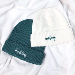 May include: Two knitted beanies, one white and one teal green, with the words "wifey" and "hubby" embroidered on them.