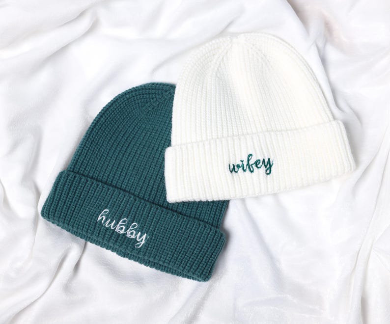 May include: Two knitted beanies, one white and one teal green, with the words "wifey" and "hubby" embroidered on them.