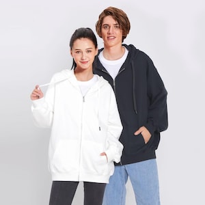 May include: Two people wearing hooded sweatshirts, one white and one black. Both sweatshirts have zipper closures.