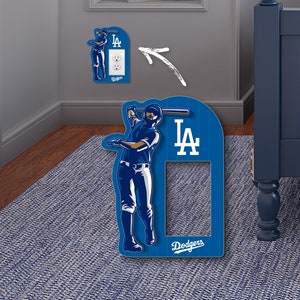 May include: A blue and white Los Angeles Dodgers light switch cover with a baseball player graphic. The cover has the team logo and the words "Dodgers" and "LA".