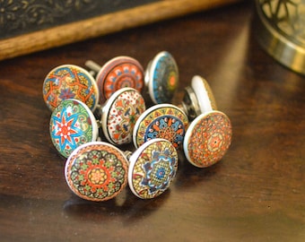 May include: A collection of ten colourful ceramic cabinet knobs with intricate patterns in shades of blue, red, orange, green, and white. The knobs are arranged in a circle on a dark brown wooden surface.