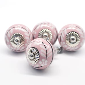 May include: Four pink ceramic cabinet knobs with white floral designs and silver accents.