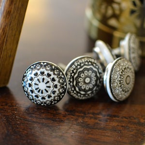 Op de afbeelding: Een set van zes zwarte en witte keramische ladeknopjes met ingewikkelde mandala-ontwerpen. De knoppen zijn rond en hebben een verhoogde rand.