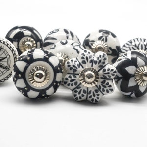 K&ouml;nnte beinhalten: Ein Satz von acht schwarzen und wei&szlig;en Keramik-Schrankkn&ouml;pfen mit verschiedenen floralen und geometrischen Designs. Die Kn&ouml;pfe haben eine silberne Metallbasis.