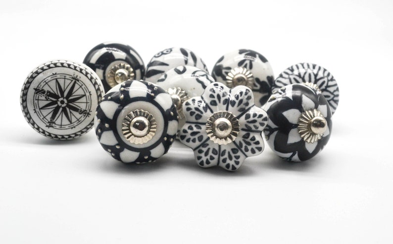 K&ouml;nnte beinhalten: Ein Satz von acht schwarzen und wei&szlig;en Keramik-Schrankkn&ouml;pfen mit verschiedenen floralen und geometrischen Designs. Die Kn&ouml;pfe haben eine silberne Metallbasis.
