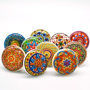 以下が含まれることがあります： 複雑な幾何学模様が施された、カラフルなセラミック製のノブ10個セット。ノブは丸型で、白地に青、緑、赤、オレンジ、黄色の様々な色合いが使用されています。