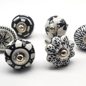 K&ouml;nnte beinhalten: Sechs schwarze und wei&szlig;e Keramikkn&ouml;pfe mit verschiedenen Mustern. Die Kn&ouml;pfe haben einen goldenen Metallakzent in der Mitte.