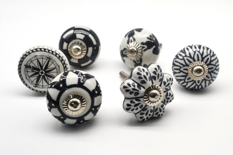 K&ouml;nnte beinhalten: Sechs schwarze und wei&szlig;e Keramikkn&ouml;pfe mit verschiedenen Mustern. Die Kn&ouml;pfe haben einen goldenen Metallakzent in der Mitte.