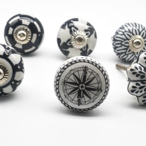 K&ouml;nnte beinhalten: Sechs schwarze und wei&szlig;e Keramik-Schrankkn&ouml;pfe mit verschiedenen Designs. Die Kn&ouml;pfe zeigen einen Kompass, geometrische Muster und florale Motive.
