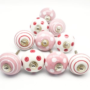May include: A set of ten pink and white ceramic cabinet knobs with red polka dots, stripes, and a gold accent.