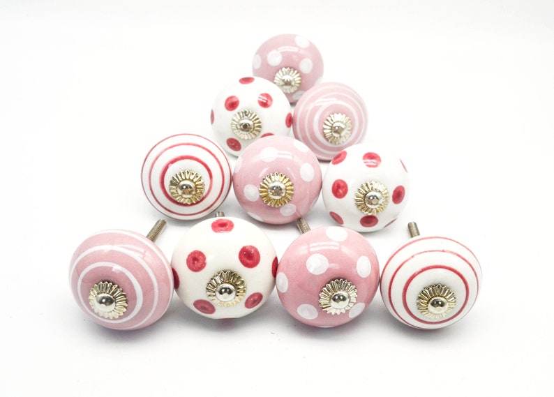 May include: A set of ten pink and white ceramic cabinet knobs with red polka dots, stripes, and a gold accent.