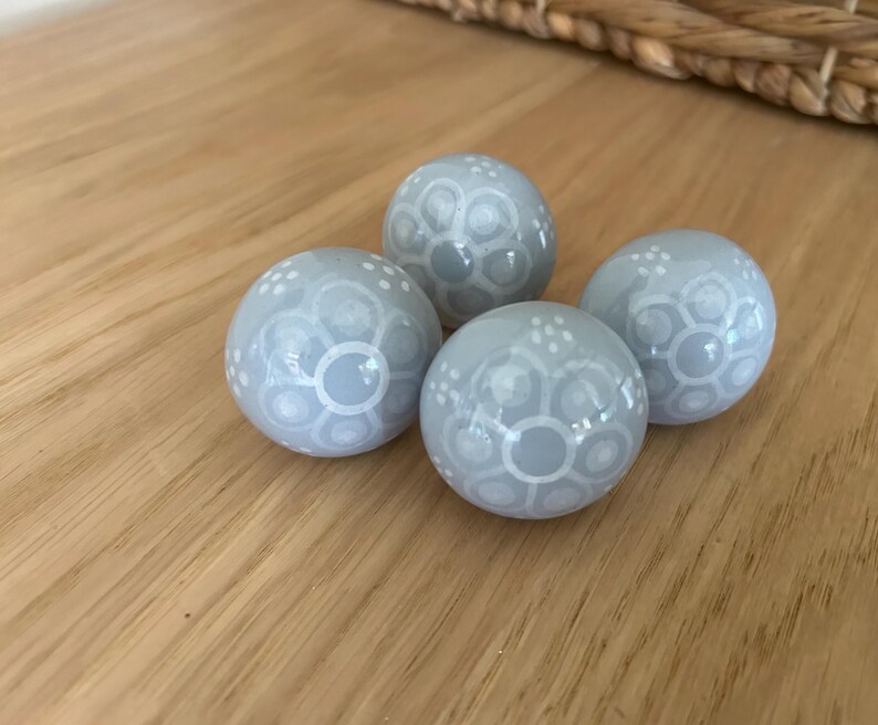 May include: Four pale blue decorative spheres with white floral patterns. The spheres are arranged on a wooden surface. The spheres have a glossy finish, possibly ceramic or glass.