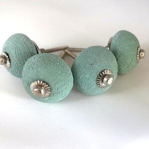 Puede incluir: Cuatro pomos de armario texturizados de color aguamarina con herrajes plateados. Los pomos son redondos con una superficie ligeramente rugosa, y los herrajes plateados tienen un dise&ntilde;o decorativo en forma de flor. Adecuado para muebles.