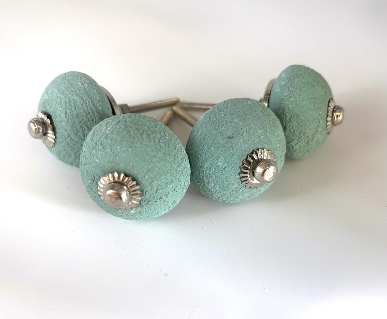 Puede incluir: Cuatro pomos de armario texturizados de color aguamarina con herrajes plateados. Los pomos son redondos con una superficie ligeramente rugosa, y los herrajes plateados tienen un dise&ntilde;o decorativo en forma de flor. Adecuado para muebles.