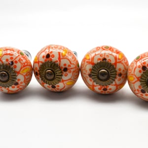 May include: Set of four ceramic cabinet knobs with a white base and orange, yellow, and brown floral pattern. Each knob has a gold-coloured metal base.