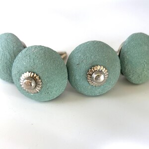 Puede incluir: Cuatro tiradores de armario de color aguamarina con superficie texturizada y herrajes plateados. Los tiradores son redondos con un dise&ntilde;o decorativo de roseta plateada. Adecuados para cajones y armarios. Cada tirador mide unos 4 cm de di&aacute;metro.