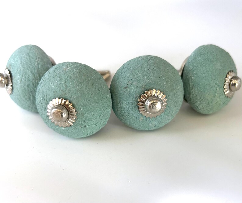 Puede incluir: Cuatro tiradores de armario de color aguamarina con superficie texturizada y herrajes plateados. Los tiradores son redondos con un dise&ntilde;o decorativo de roseta plateada. Adecuados para cajones y armarios. Cada tirador mide unos 4 cm de di&aacute;metro.